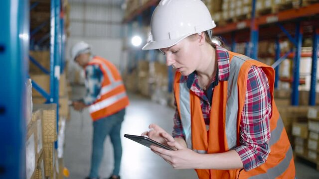 A Caucasian female worker using a digital tablet checking the cardboard box on the shelf in the distribution warehouse