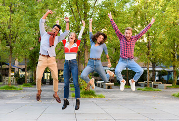 Group of exuberant young friends cheering and leaping in air - obrazy, fototapety, plakaty
