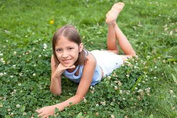 A little teenage girl in a T-shirt and shorts in a clearing with green grass enjoys summer on a sunny day, looks at the camera and smiles. Happy childhood. Summer holidays