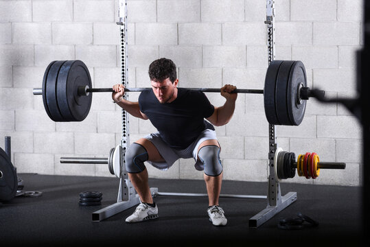 Young man performing heavy back squats exercise in gym