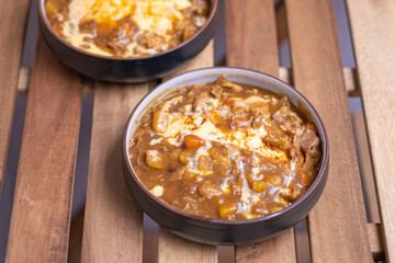 Delicious Japanese sliced meat curry serve with omlete rice and vegetables, curry Rice in black plate on a wooden table with copy space.