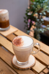 Hot coffee with milk in a glass on a wooden table with nature background. Cafe latte macchiato layered coffee, Copy space.