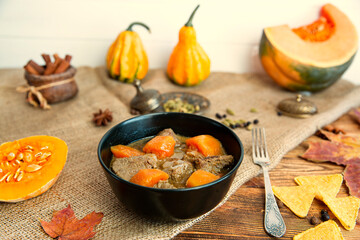 Tasty meat dish with pumpkin, autumn warm meal on brown wooden table, top view. 