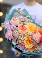 Strong man holding a delicate bouquet of beautiful flowers in his hands. Colorful flower bouquet. Wrapped flowers bouquet.
