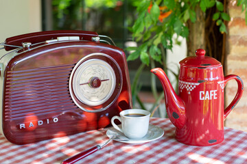 A white cup with coffee stands near a coffee pot and a radio in a retro style on a table in a summer garden. Outdoor breakfast theme.