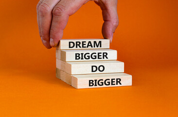 Dream and do bigger symbol. Concept words 'Dream bigger do bigger' on wooden blocks on a beautiful orange background. Businessman hand. Business, motivational and dream and do bigger concept.