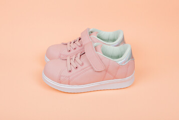 Cute pink children's sneakers. Orange background. Baby clothes and shoes