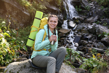 Naklejka na ściany i meble Tourist with vacuum flask near waterfall in mountains
