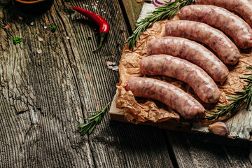 raw breed butchers sausages in skins with herbs and rosemary on a wooden background. Sausages for...