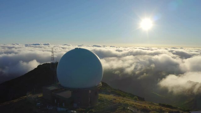 Meteorological weather radar station with a large white sphere on top of a mountain over a clouds at dawn. Aerial panoramic view