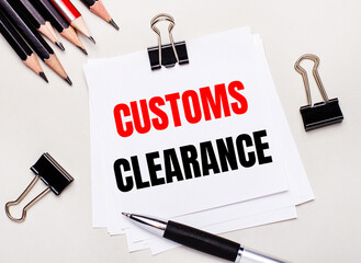 On a light background, black pencils, black paper clips, a pen and a sheet of white paper with the text CUSTOMS CLEARANCE