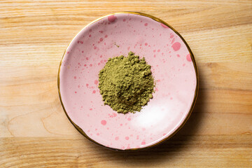Pile of green kratom powder in a small ceramic rose plate on the wooden texture photo from top flat...