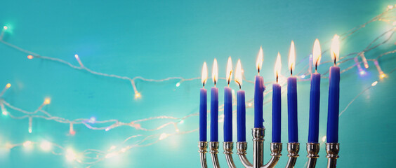 Image of jewish holiday Hanukkah with menorah (traditional candelabra) and candles over garland glitter lights background