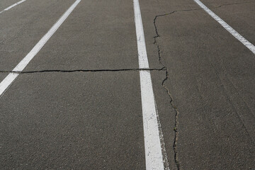 Photo of gray asphalt road with cracks and white markings