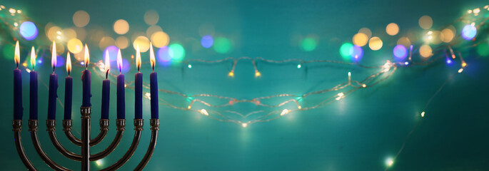 Image of jewish holiday Hanukkah with menorah (traditional candelabra) and candles over garland...