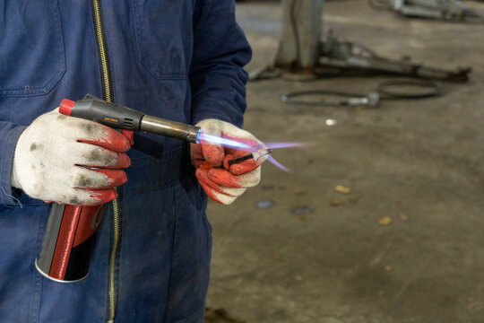 Car master mechanic with gas torch repair heating handmade tool for repairing and restoring car parts in vehicle repair service. Creation of a handmade tool.