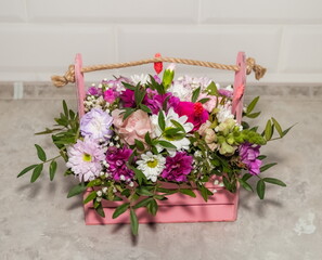 Multicolored flowers of roses and chrysanthemums close-up in a pink wooden basket on a white background