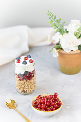 Toasted muesli or homemade granola with nuts and yogurt and berries in small glass jar with a spoon on gray background
