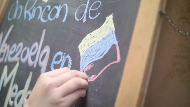 Close-Up of a Female Hand Writing "A Venezuelan Spot in Medellin" with Chalk on a Blackboard