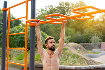 Obraz premium Athletic sportsman trains on the horizontal bars. Training at the open air sprorts ground.