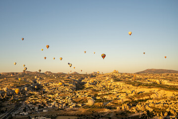Sunrise view of unusual cityscape. Colorful hot air balloons fly in blue sky over amazing valleys and cities.