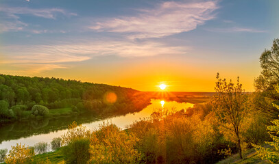 Plakat Scenic view at beautiful spring sunset on a shiny river valley with green branches, trees, bushes, grass, golden sun, calm water ,deep blue cloudy sky and forest on a background, spring landscape