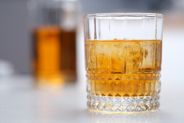 Glass of whiskey with ice standing on table closeup