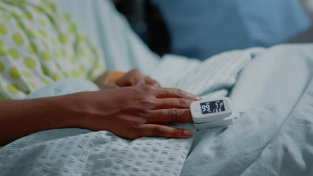 Close up of oximeter on finger of patient with illness in hospital ward bed. Sick woman having tool to measure oxygen saturation and pulse pressure to cure disease. Medical care