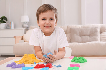 Cute little boy playing with bright kinetic sand at table in room