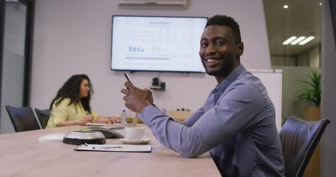 Portrait of smiling african american businessman using smartphone looking at camera in modern office