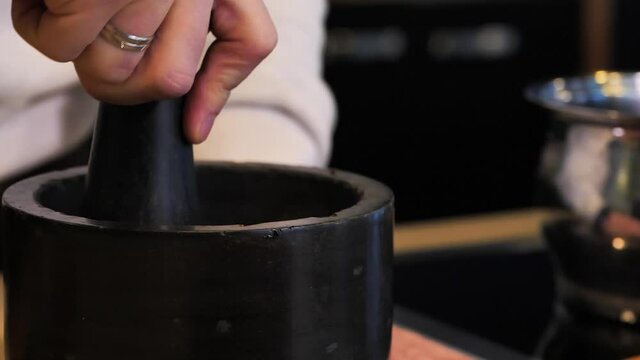 Male hands grind black pepper in granite mortar