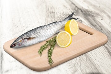 Fresh raw Fish decorated with herbs and vegetables on a wooden pad.
