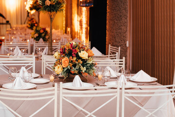wedding decoration - table set with plates, cutlery and glasses with white, yellow and orange flowers