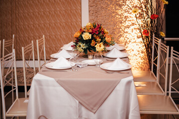 wedding decoration - table set with plates, cutlery and glasses with white, yellow and orange flowers