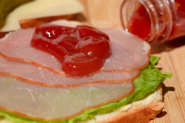 Toast with ham and a leaf of green lettuce poured with ketchup on a wooden background.