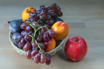 red grape berries and fresh fruits in a straw basket on a light wooden background