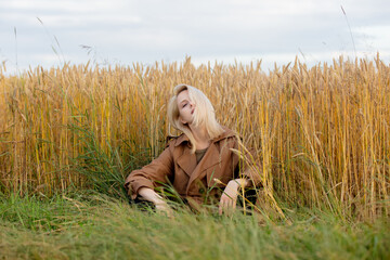 Blonde woman in cloak is sitting near wheat field