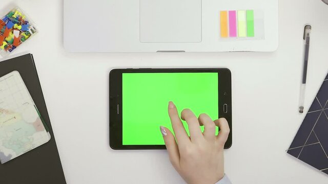 Top view a designer girl is sitting at a table with a tablet on the chromakey screen, various office supplies are lying on the table