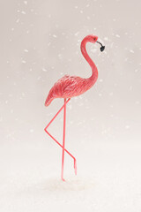 Snowing minimal concept. A pink toy flamingo standing alone while snowflakes falls around, light gray