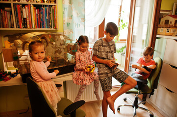 Four children holding their favorite pets on hands. Kids playing with hamster,turtle and parrots at home.