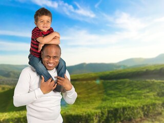 Happy father carrying son on back having fun outdoors in a park