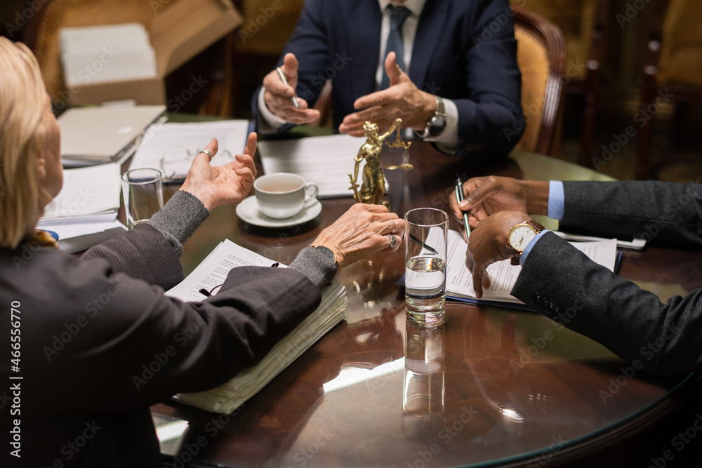 Poster hands of three contemporary intercultural lawyers during discussion of working points by table with 