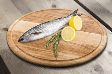 Fresh raw Fish decorated with herbs and vegetables on a wooden pad.