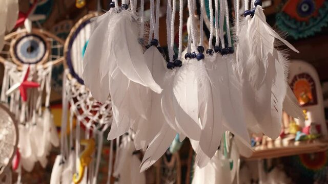 Close-up view 4k stock video footage of many cute white totem dream catchers with white featheres hanging outside of store of souvenirs in Turkey