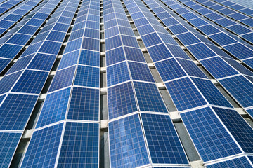 Obraz premium Aerial view of solar power plant with blue photovoltaic panels mounted on industrial building roof for producing green ecological electricity. Production of sustainable energy concept.