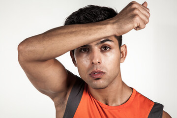 Portrait of exhausted athletic young man standing with hand on forehead, looking at camera, being tired after workout, looking at camera. Indoor studio shot isolated on gray background.