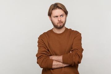 Portrait of handsome man with beard wearing sweatshirt, standing, crossed arms, looking away and...