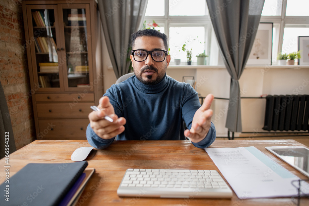 Poster confident middle-aged man in eyeglasses and blue pullover explaining subject to online audience in f