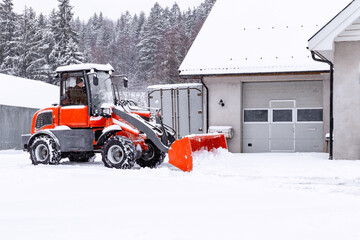 Man on red tractor with snowplow removing snow during the snowfall.  Blizzard weather conditions....