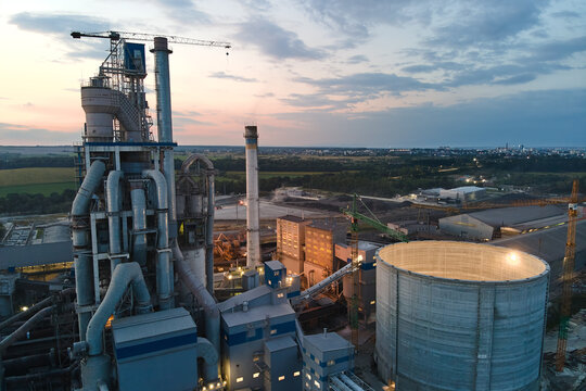 Aerial view of cement factory with high concrete plant structure and tower cranes at industrial production area at night. Manufacture and global industry concept.